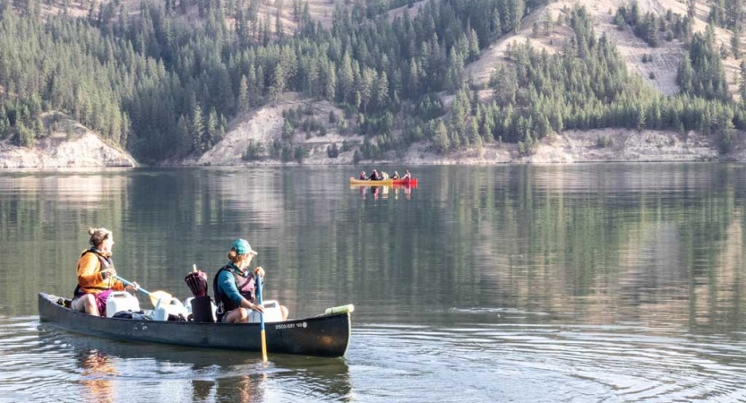 two girls paddle a canoe on still water. there is another canoe in the background